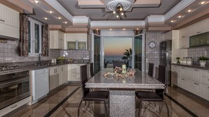 A modern kitchen with granite countertops, stainless steel appliances, and a dining area with a glass-top table and chairs. - Frido Luxury Villa (Zakynthos)
