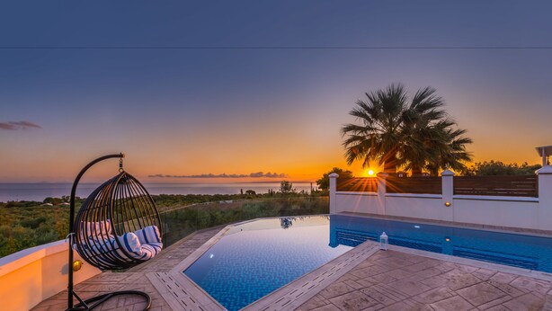 Una piscina con una hamaca y vistas a la puesta de sol sobre el mar.