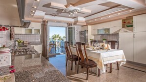 A modern kitchen with granite countertops, white cabinetry, and a dining area with a table set for four. - Frido Luxury Villa (Zakynthos)