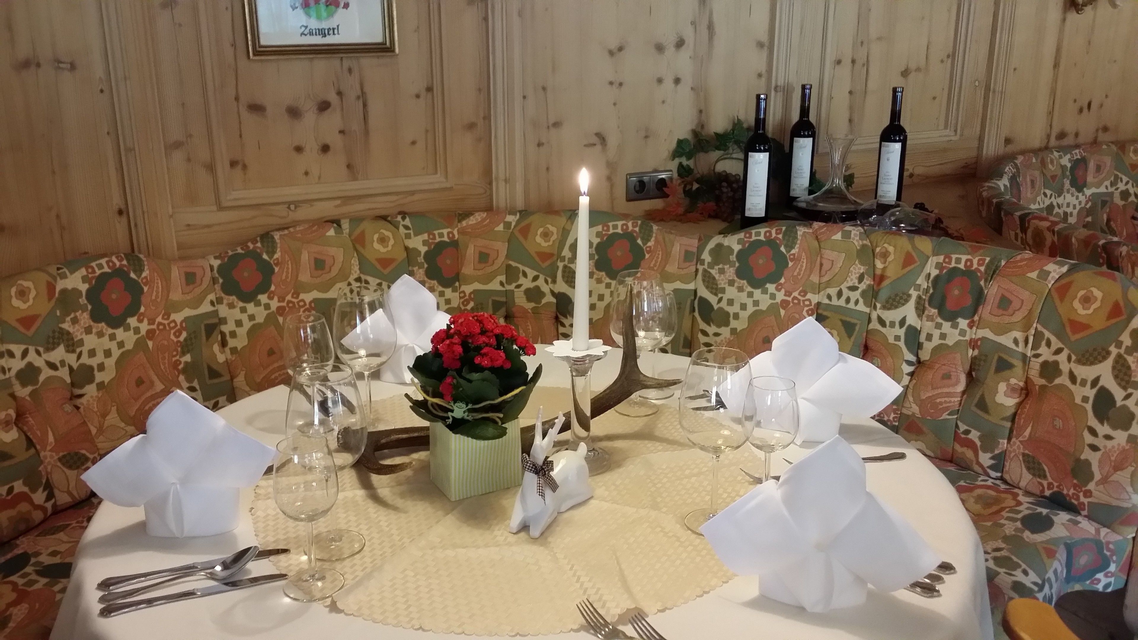 A dining table set with wine glasses, a candle, and a vase of red flowers.