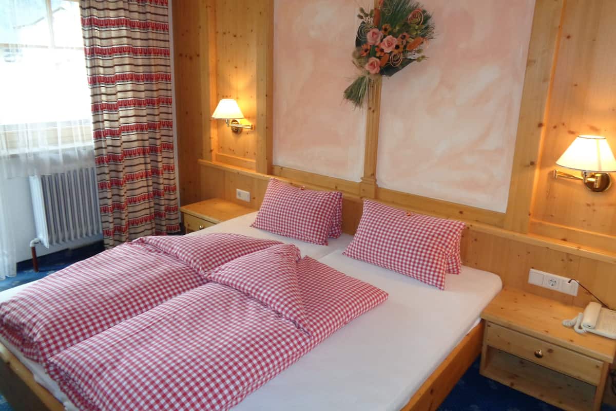 A hotel room with a wooden bed, checkered bedding, two bedside lamps, a wall-mounted flower arrangement, and a radiator.