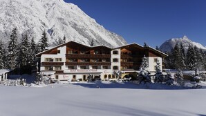 Een hotel met meerdere balkons, een met sneeuw bedekte berg op de achtergrond en een heldere blauwe lucht.