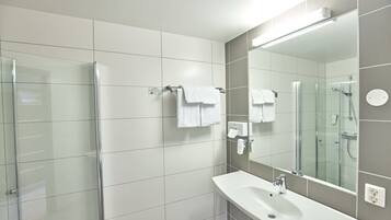 A modern bathroom with a glass shower enclosure, a white sink, and a large mirror.