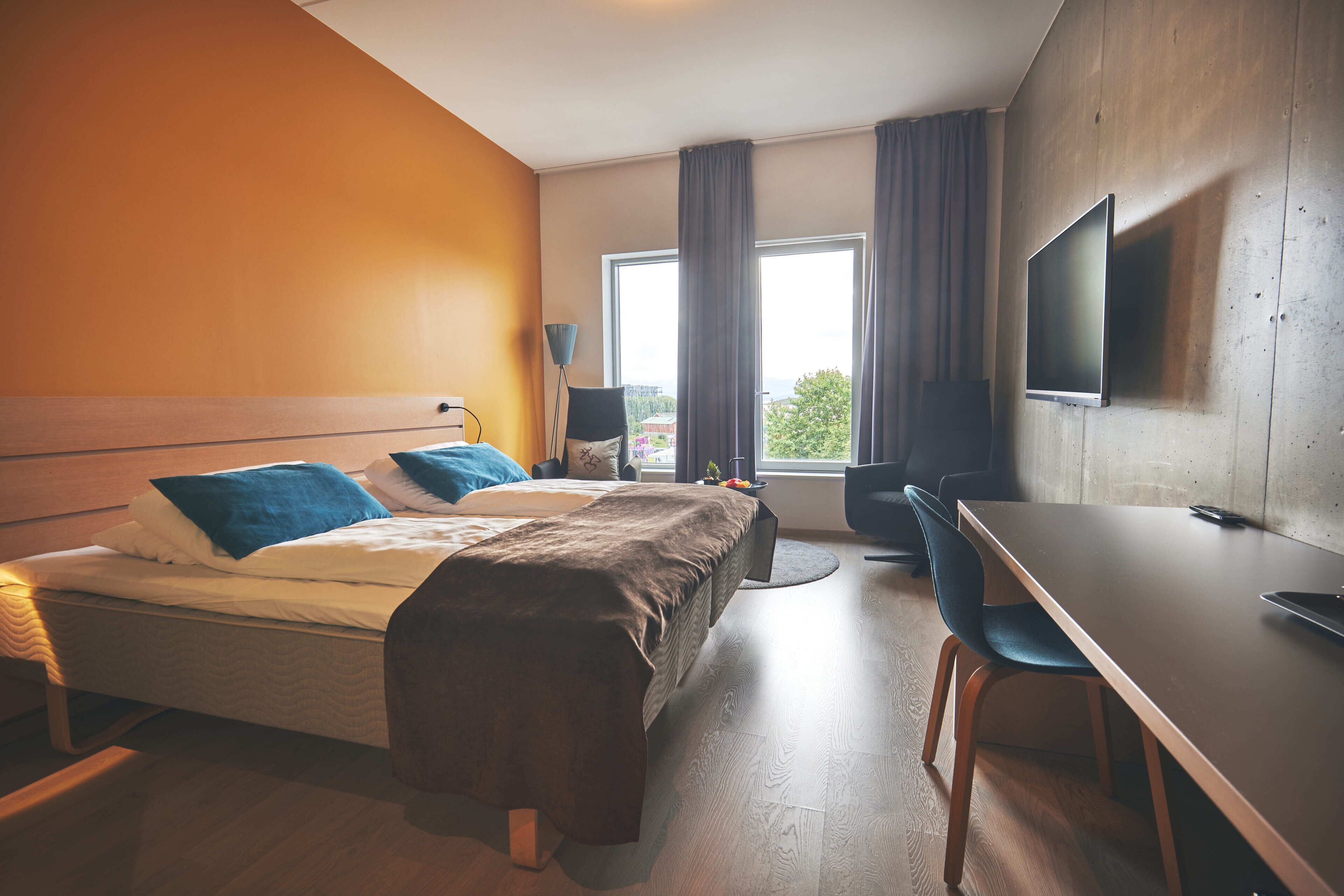 A hotel room with a bed, a desk, a chair, a TV, and a window with curtains.