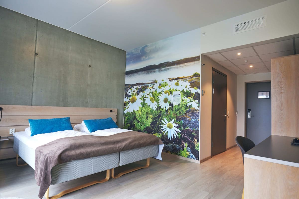 Ein modernes Hotelzimmer mit einem großen Bett, einem Schreibtisch und einem Wandgemälde mit Blumen.