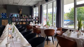 Un restaurante con una mesa larga dispuesta para comer, una estantería y un amplio ventanal con vistas al exterior.