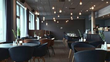 A modern restaurant interior with round tables, dark chairs, hanging pendant lights, and a bar area.