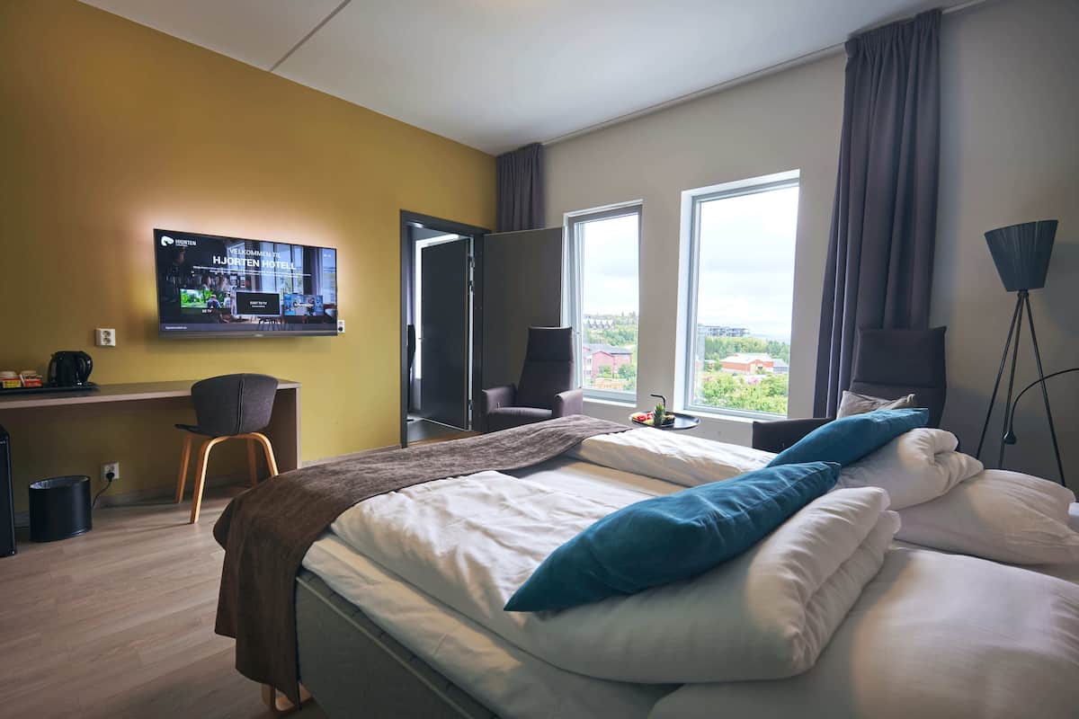 Ein modernes Hotelzimmer mit Bett, Schreibtisch, Stuhl, Fernseher und einem Fenster mit Blick.