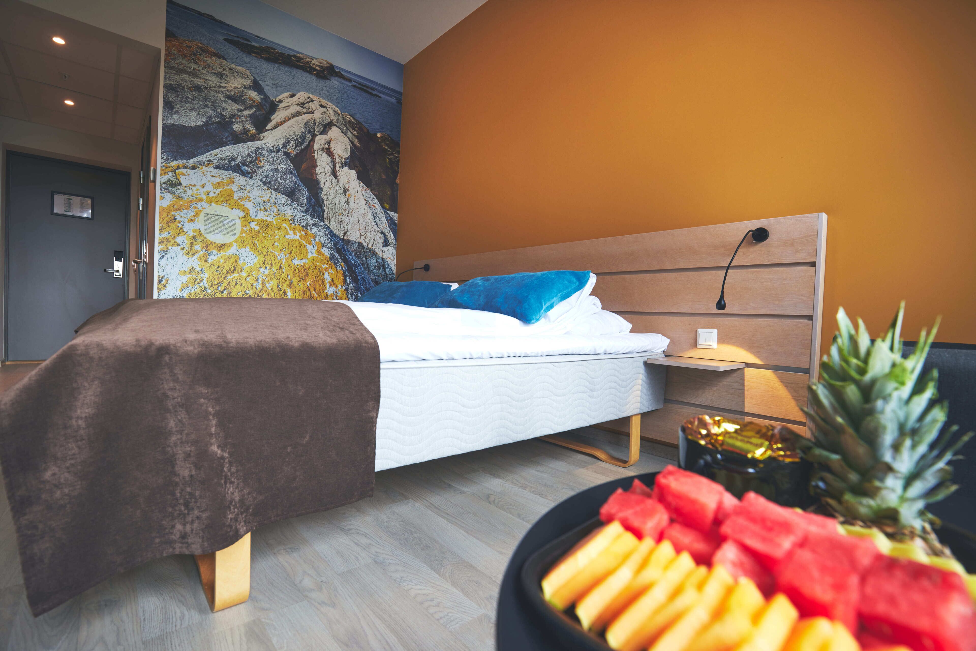 A modern bedroom with a large bed, a nightstand, a fruit bowl, and a mural on the wall.