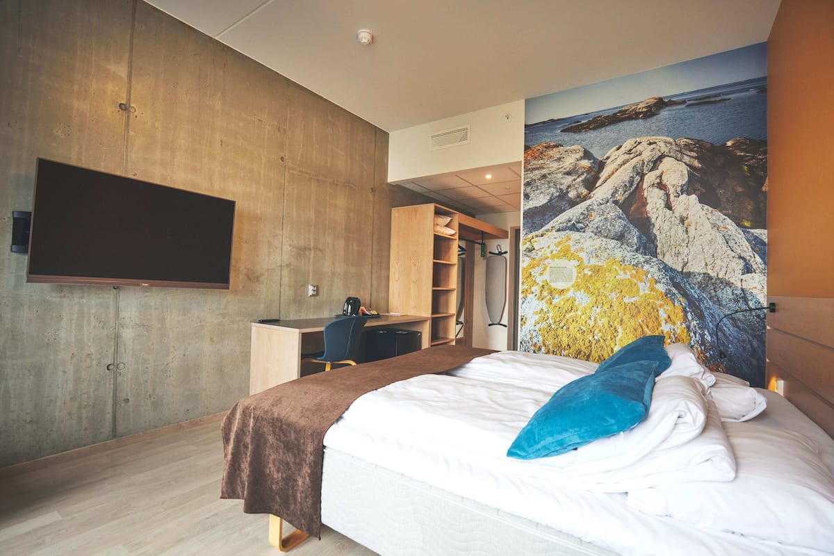 Ein modernes Hotelzimmer mit einem großen Bett, einem Schreibtisch und einem an der Wand befestigten Fernseher.