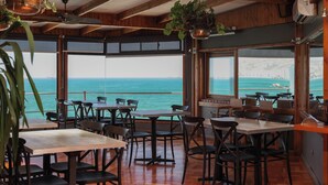 Restaurante com interiores em madeira, janelas amplas e vista para o mar.