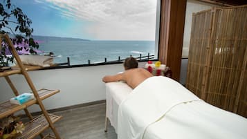 Relax in a serene room with a large window overlooking the sea, featuring a comfortable bed and a tranquil bamboo shelf with a decorative plant.