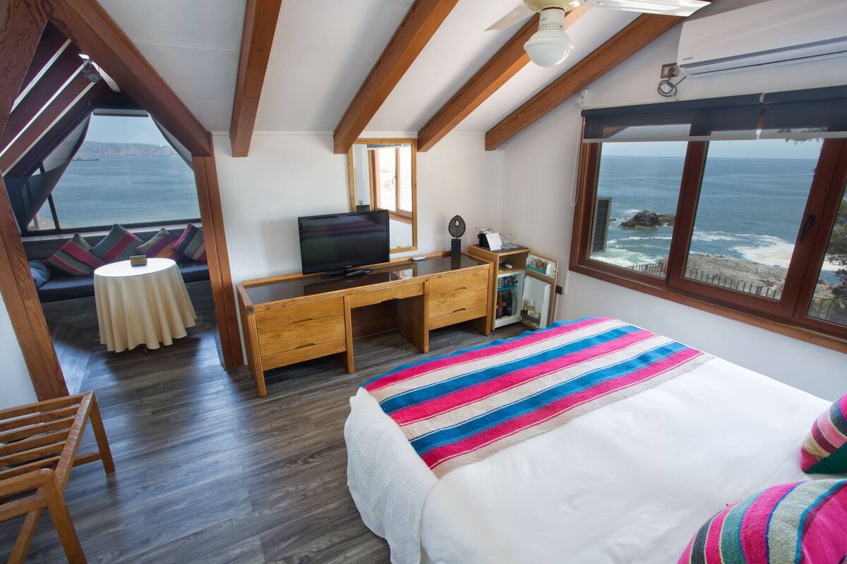 Un dormitorio con cama, escritorio, televisor y vista al océano.