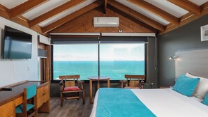Quarto com cama grande, escrivaninha e televisão. Tem vista para o mar.
