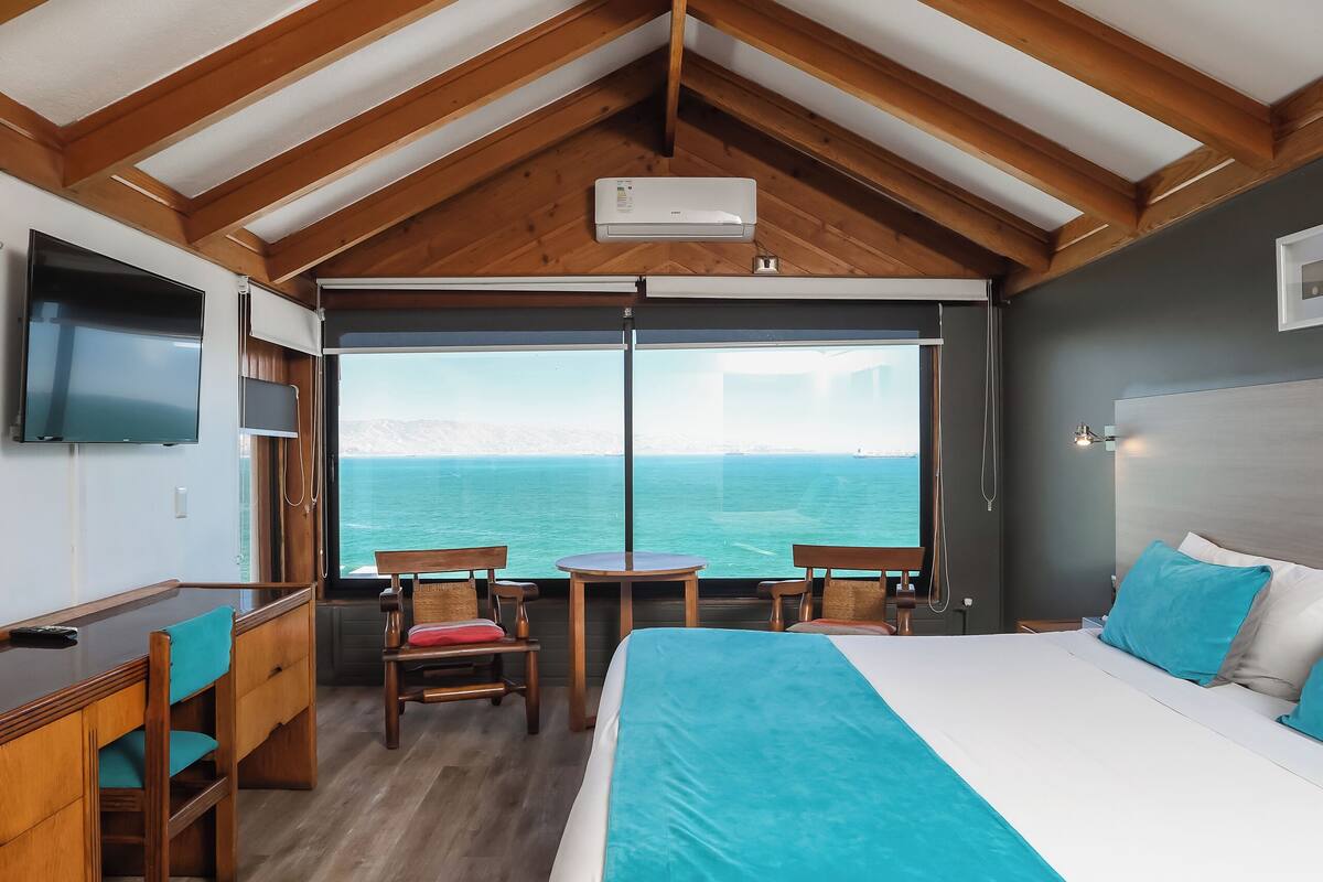 Un dormitorio con una cama grande, un escritorio y un televisor. Tiene vista al mar.