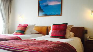 Uma cama de casal com duas almofadas coloridas, um quadro na parede acima e um telefone na mesa de cabeceira.
