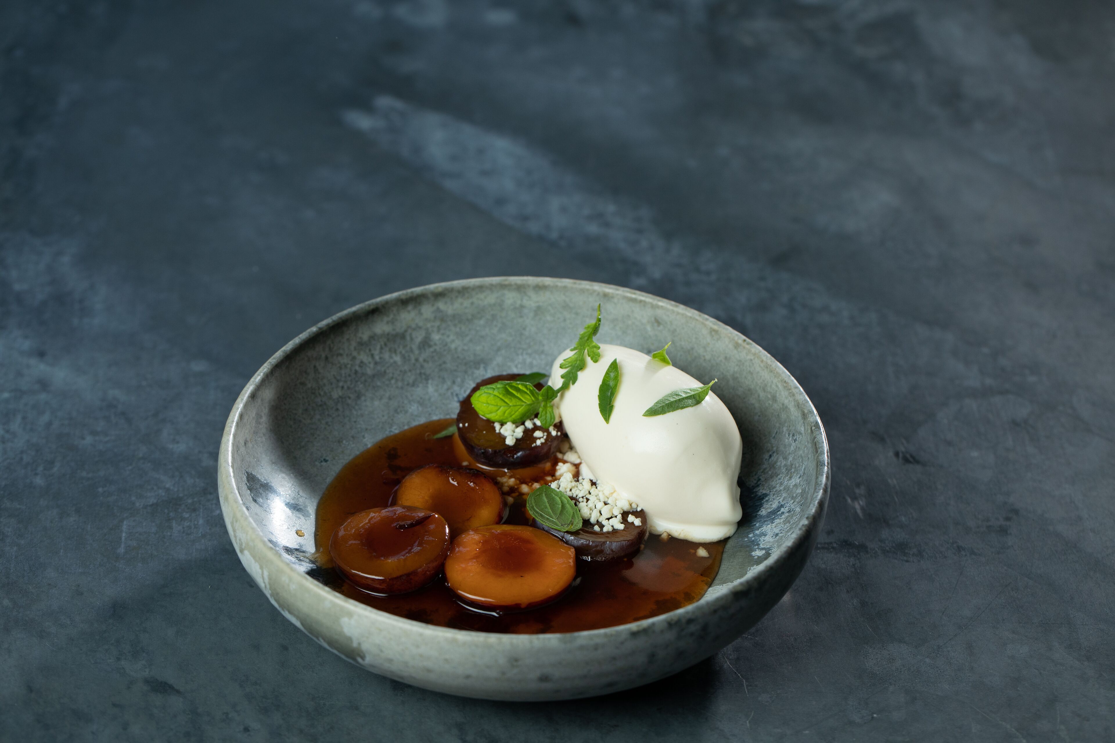 A bowl of food with a dollop of cream and mint leaves on a textured surface.