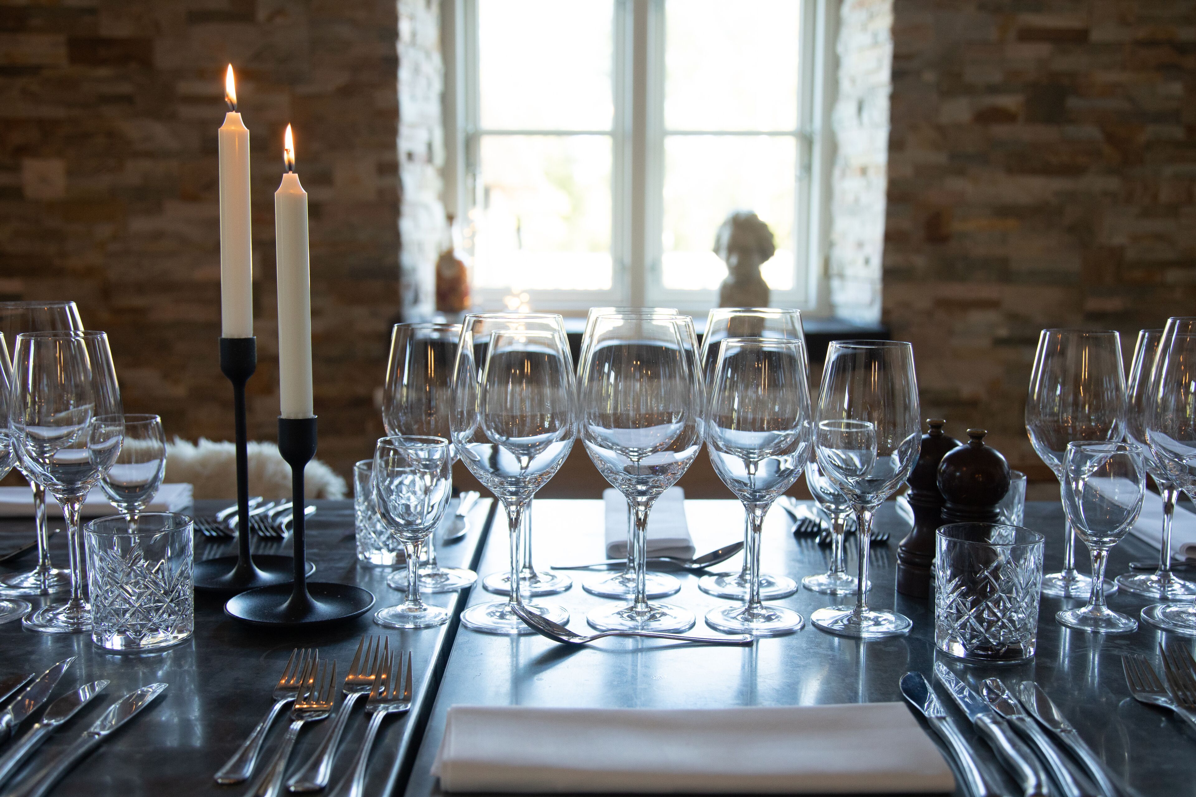 Una mesa servida para una comida con copas de vino, cubiertos y velas.