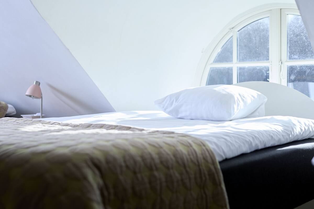 A bedroom with a bed, a bedside lamp, and a window.