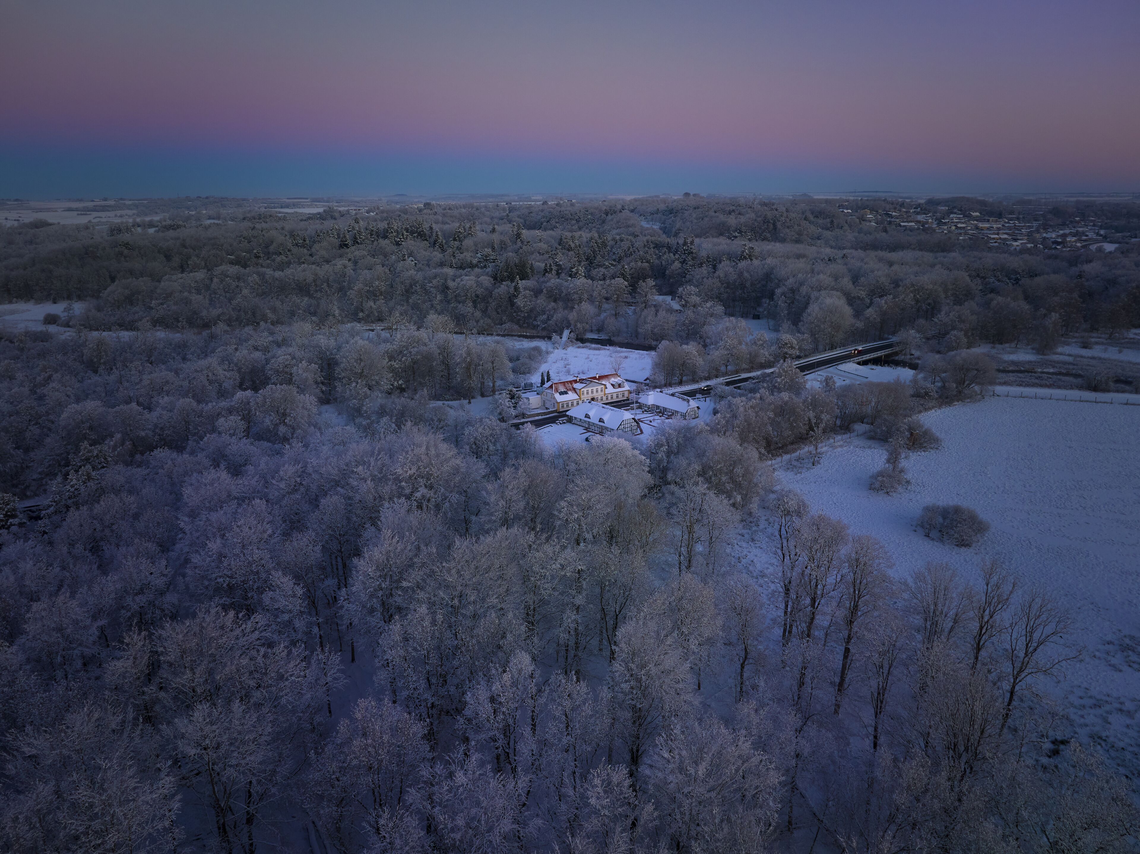 A snow-covered landscape with a building complex surrounded by trees.