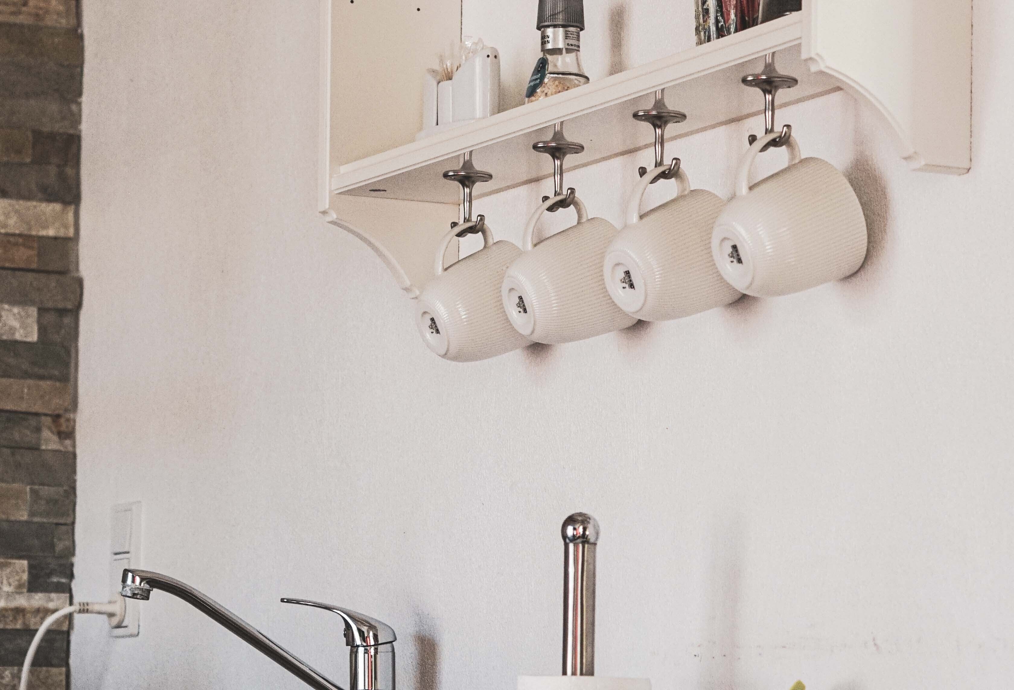 A kitchen with a white countertop, a stainless steel faucet, and a hanging rack with white mugs.