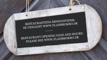 Un letrero de madera con información sobre los días y horarios de apertura de un restaurante.