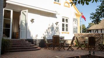 En vit byggnad med en stenmur, utomhusplats med trästolar och bord samt en flagga.