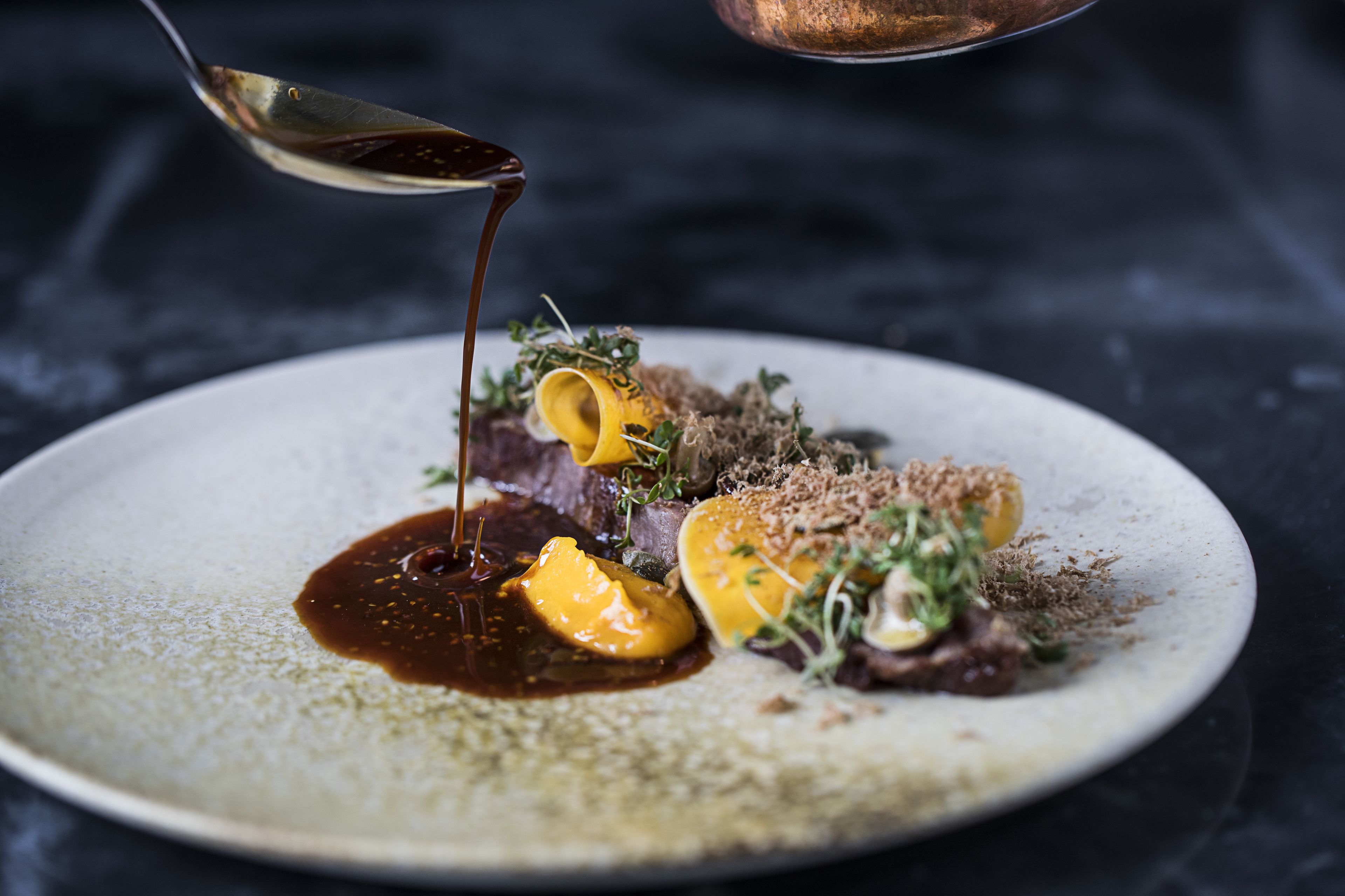 A plate of food with a spoon pouring sauce over it.
