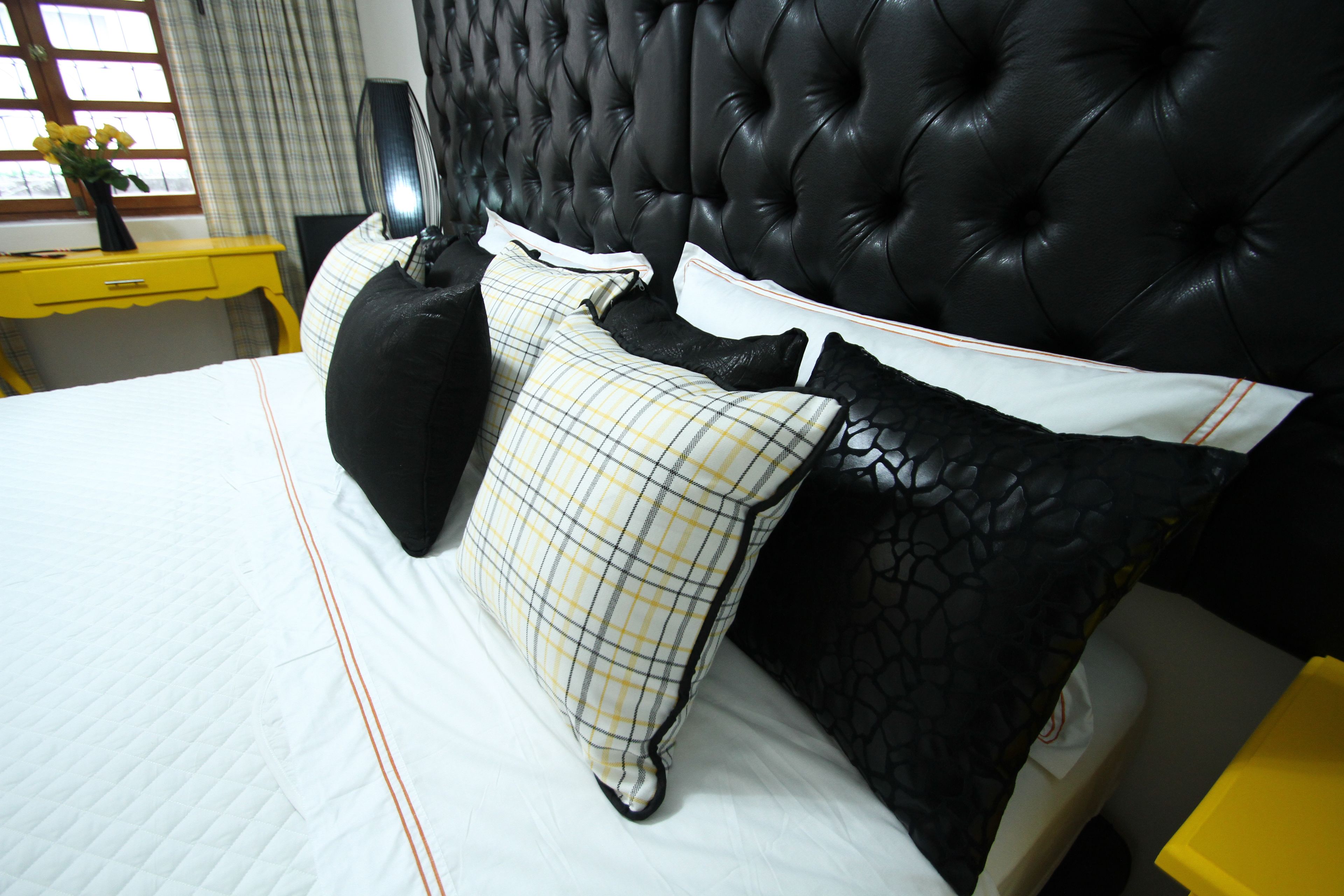 A neatly made bed with a black headboard, a yellow bedside table, and a window with curtains.