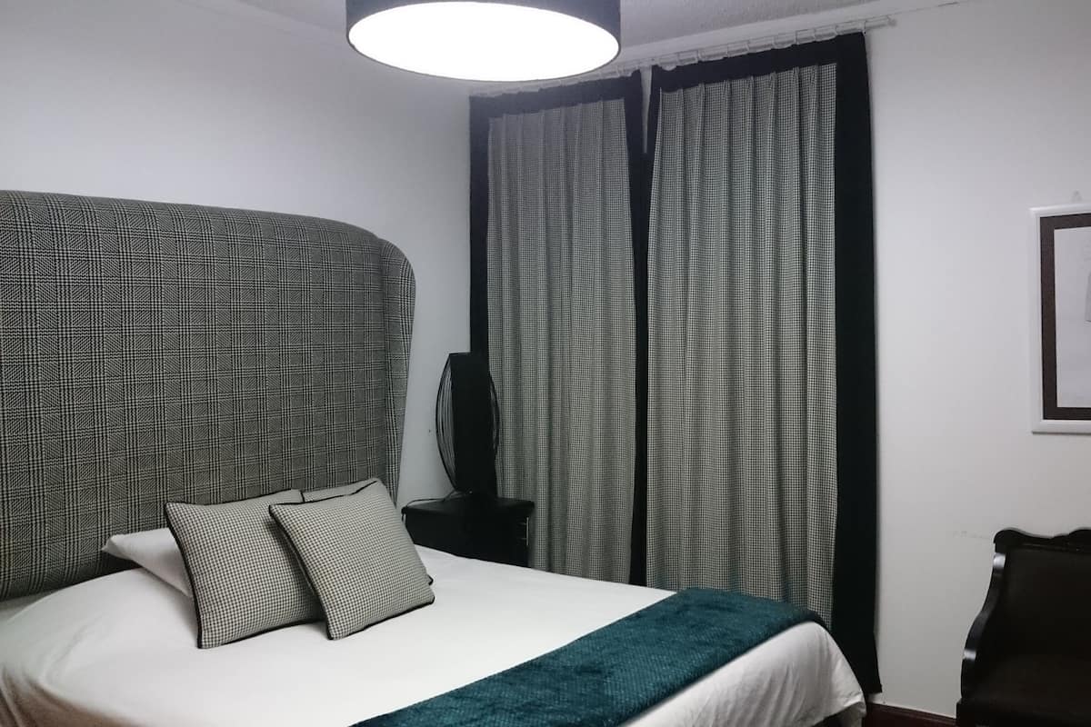 Une chambre à coucher avec un lit, des oreillers, un bureau, une chaise, une lampe et un tableau encadré accroché au mur.