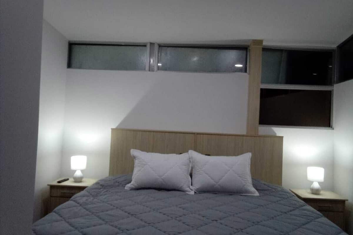 Une chambre à coucher avec un lit, deux lampes de chevet, une tête de lit en bois et une fenêtre située au-dessus du lit.