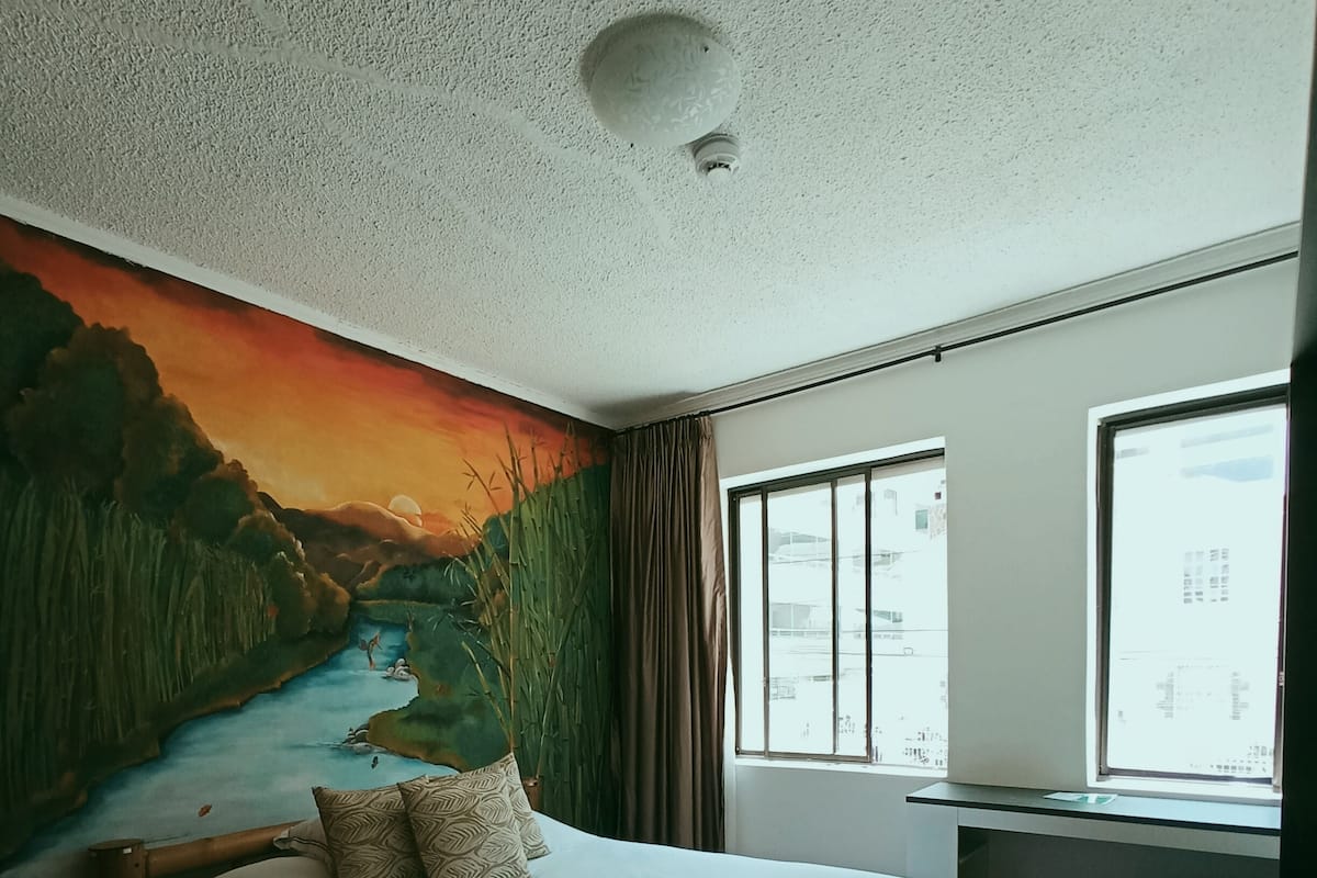 Une chambre à coucher avec un lit, une fresque murale, un bureau et une fenêtre.