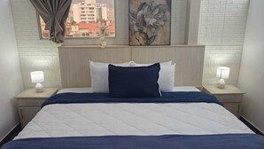 A hotel room with a bed, two bedside lamps, a window with curtains, and a cityscape view. - Hotel + Arte (Quito)