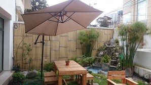 A wooden table and chairs under a large umbrella in a garden area with a bamboo fence, a small pond, and various plants. - Hotel + Arte (Quito)