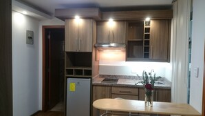 A compact kitchen with wooden cabinets, a built-in stove, and a small refrigerator. - Hotel + Arte (Quito)
