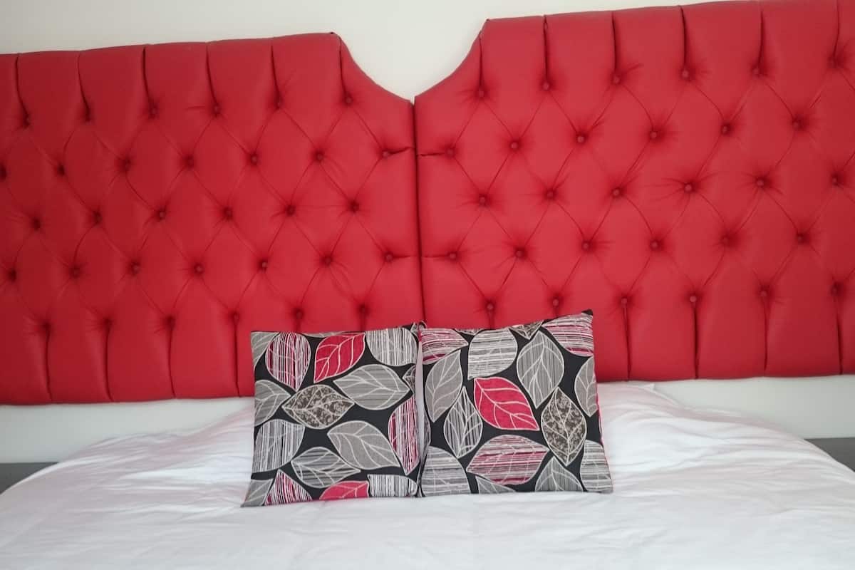 Un lit avec une tête de lit rouge à motifs capitonnés et deux coussins à motifs.