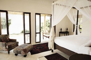 A bedroom with a four-poster bed, a patterned armchair, and a bench by the window.