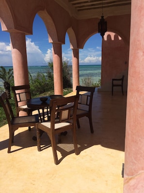 An outdoor patio with a table and chairs, overlooking a beach with clear blue water. - Qambani Luxury Resort (Michamvi)