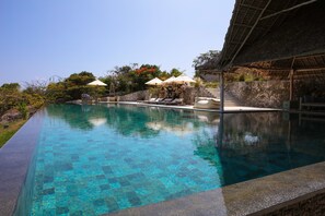 A clear pool with lounge chairs and umbrellas, surrounded by greenery and a stone wall. - Qambani Luxury Resort (Michamvi)