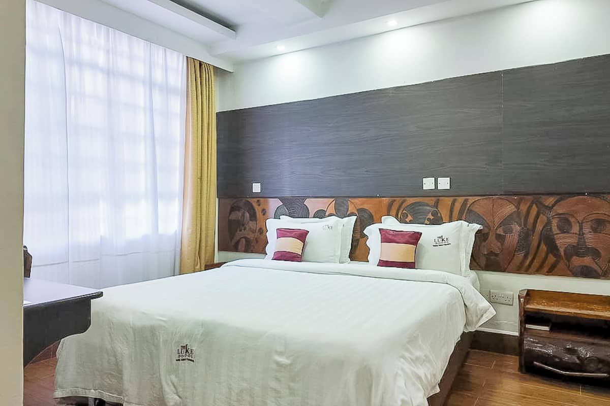 A hotel room with a bed, a nightstand, a wooden headboard, and a window with curtains.