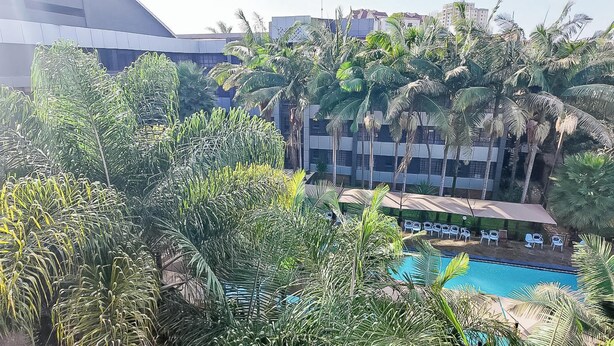 A pool surrounded by palm trees and a building with multiple balconies. - The Luke Hotel (Nairobi)