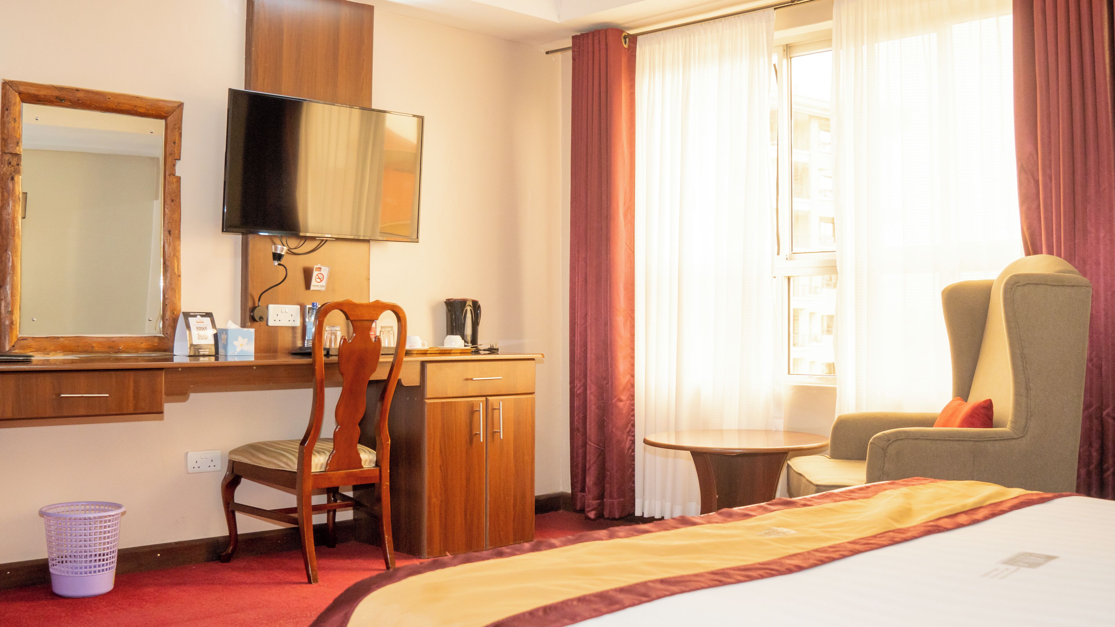A hotel room with a bed, a desk with a chair, a television, and a window with curtains.
