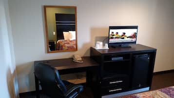 A hotel room with a desk, a television, a telephone, and a mirror.