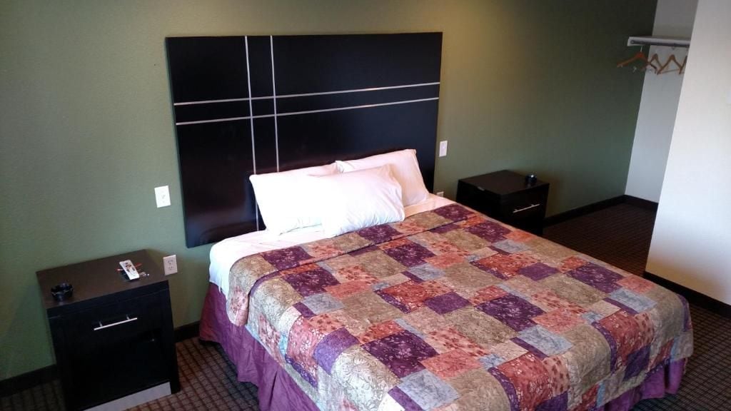 Une chambre d’hôtel comprenant un lit, deux tables de chevet, une petite table et une étagère fixée au mur.