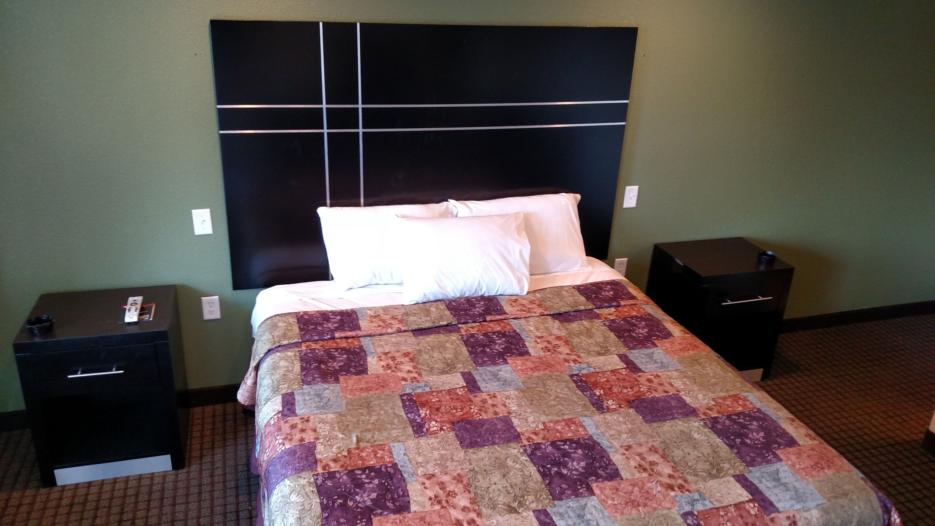 A hotel room with a large bed, a headboard, two nightstands, and a quilt.
