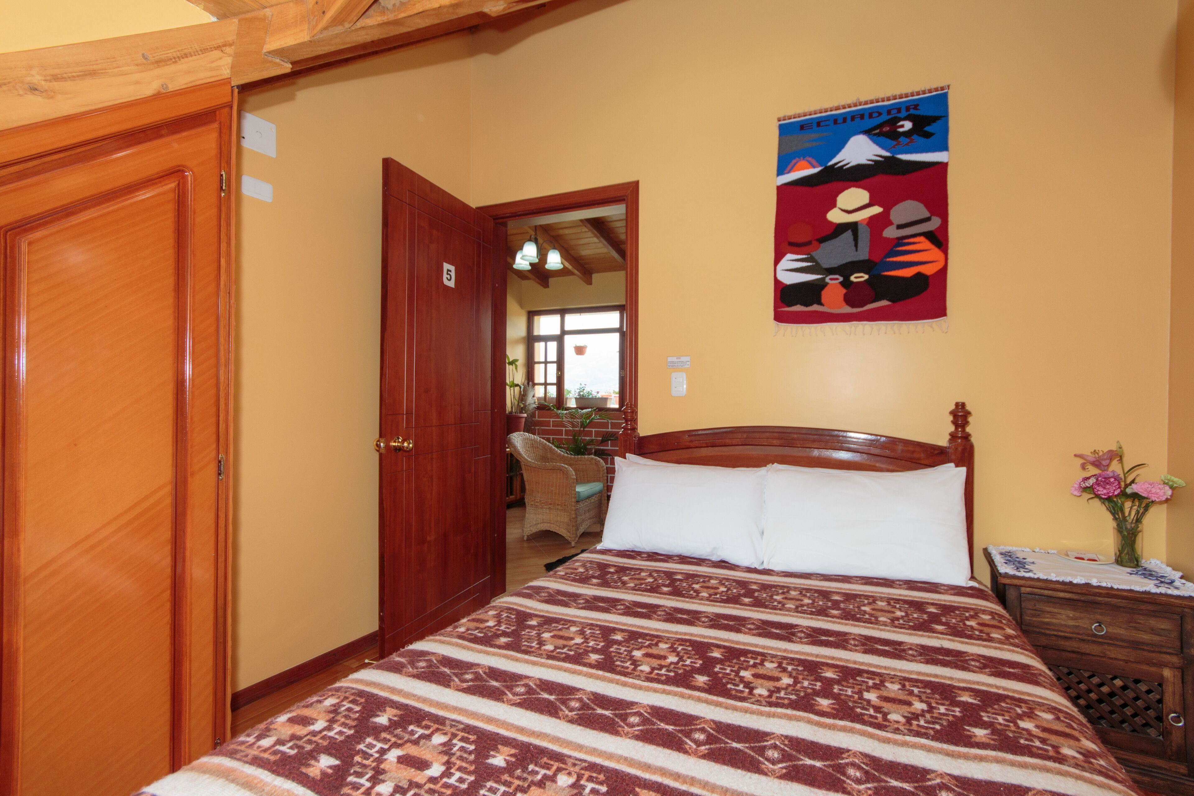 Un dormitorio con una cama de madera, un armario de madera, un cartel en la pared y una mesita de noche con un jarrón de flores.