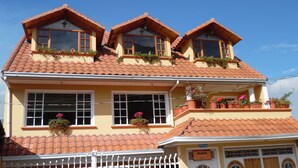 A building with a tiled roof, multiple windows, and balconies with potted plants. -  Casa de Hu éspedes Casa de Luis (San Pablo del Lago)