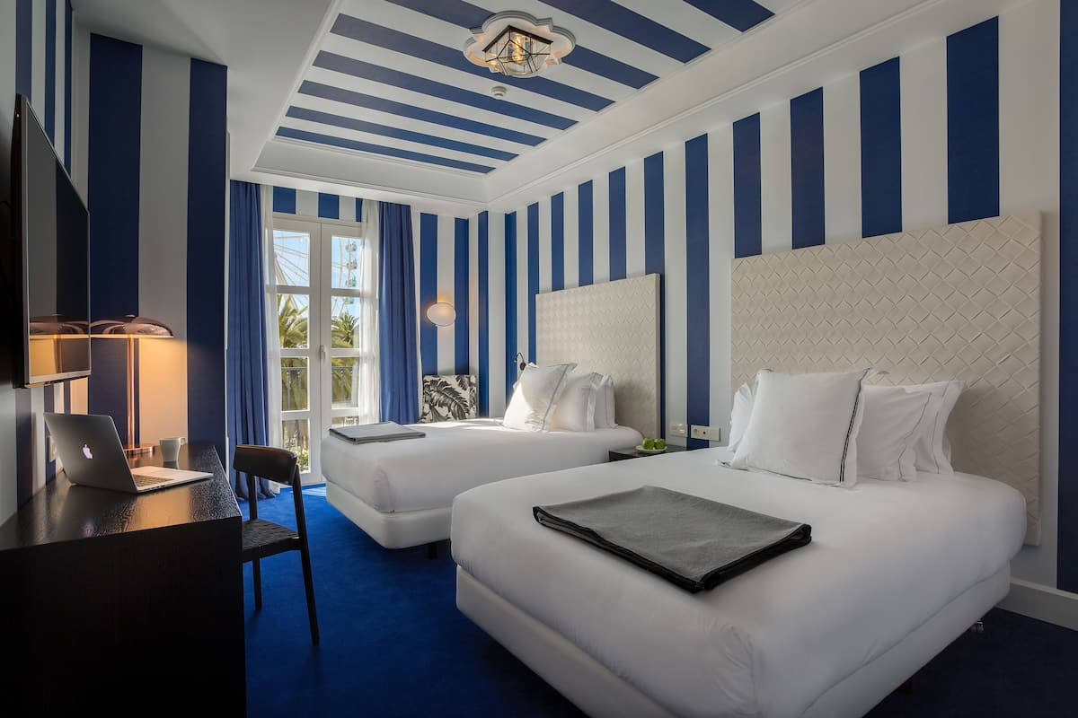 Habitación de hotel con dos camas, un escritorio con una computadora portátil y vistas al exterior.
