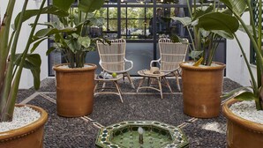 Un balcón con plantas en macetas, sillas de mimbre y una fuente decorativa.
