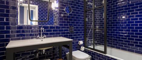 A bathroom with blue-tiled walls, a white sink, a toilet, and a shower area.